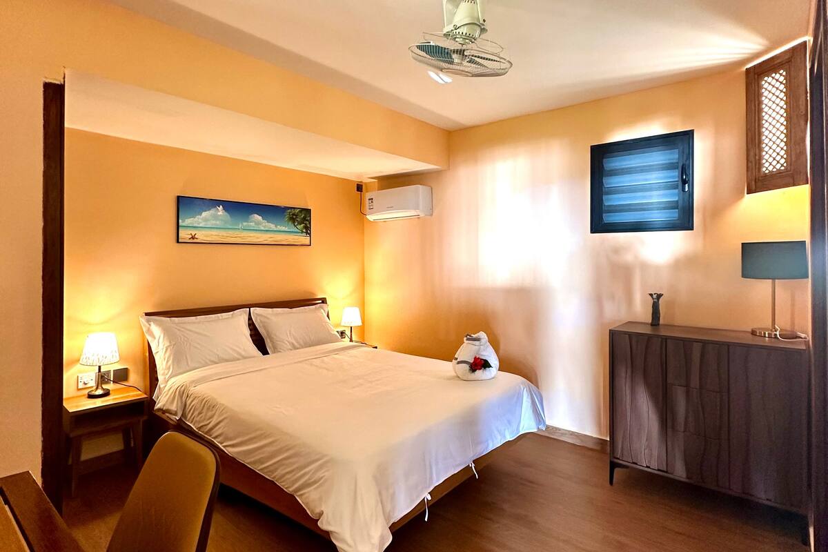 A hotel room with a bed, bedside table, chair, and a TV on the wall.