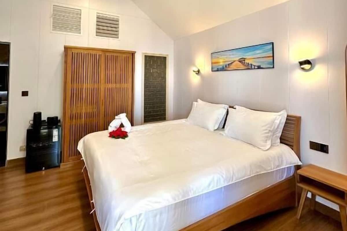 A spacious bedroom with a large bed, wooden flooring, a wooden wardrobe, and a painting on the wall.