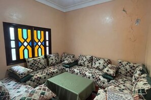Ein Zimmer mit einer Couchgarnitur mit Muster, einem kleinen Tisch und einem Fenster mit geometrischem Buntglasdesign.