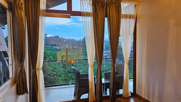 Una habitació amb un finestra gran, cortines i vista a un paisatge verd.