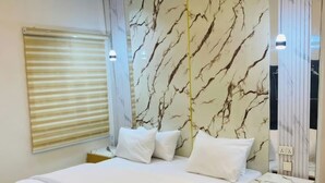 A modern bedroom with a marble-patterned headboard, a large bed with white bedding, and a bedside table with a lamp.