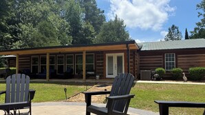 Un espace patio aménagé avec des fauteuils Adirondack, une table en pierre et un bâtiment en bois doté d’un porche couvert.