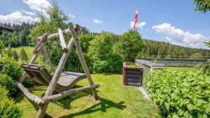 A wooden swing in a lush garden with a flag in the background. - Double Room 1 at Gästehaus Elisabeth with Mountain View, Shared Pool and Wi-Fi (Löbenau)