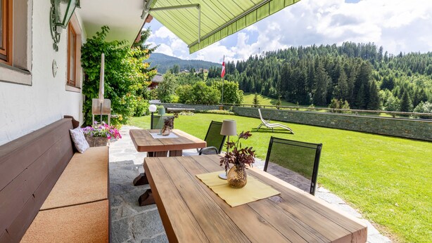 A covered patio with wooden furniture, a stone bench, and a view of a forested valley. - Double Room 1 at Gästehaus Elisabeth with Mountain View, Shared Pool and Wi-Fi (Löbenau)