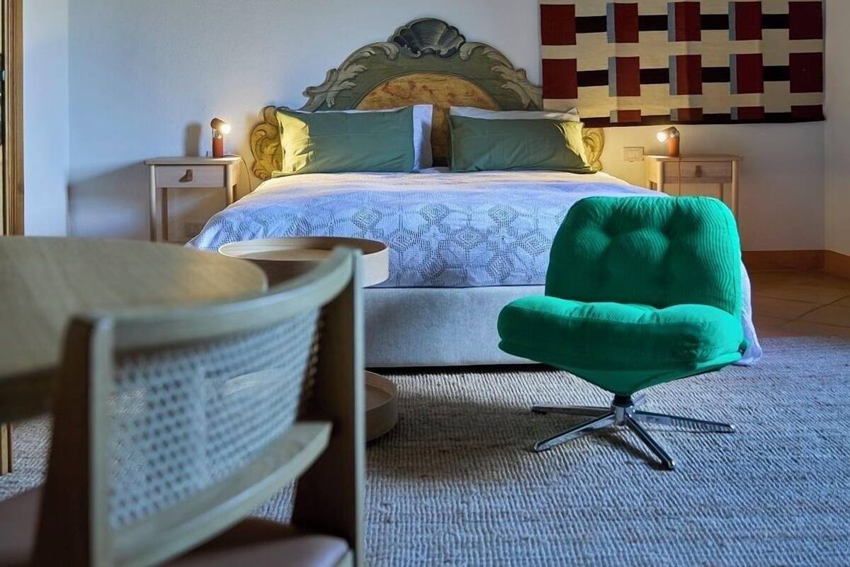 Ein Schlafzimmer mit einem Bett, einem grünen Sessel, einem Nachttisch und einer Wanddekoration.