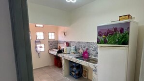 Une cuisine de taille réduite, avec un sol carrelé, un réfrigérateur blanc, un évier et une fenêtre équipée de stores.