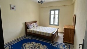 Une chambre à coucher avec un lit, une armoire en bois, un lustre, une fenêtre et une porte.