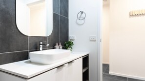 A modern bathroom with a white sink, dark tiled walls, and a large mirror. - Oak & Ivy on Windsor (Williamstown)