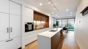 A modern kitchen with white cabinetry, a central island, and a built-in oven. - Oak & Ivy on Windsor (Williamstown)