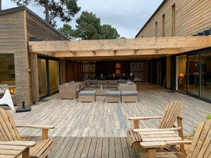 Un patio al aire libre con mobiliario de madera, incluyendo sofás y sillas, y una estructura de pérgola.