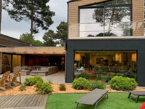 Una casa moderna con terraza de madera, mobiliario exterior y puerta de cristal que da a una sala de estar.