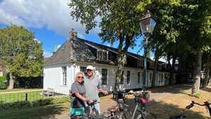 Ein traditionelles Gebäude mit einem Stein-Dach und weißen Wänden, umgeben von Bäumen und einem gepflasterten Weg.