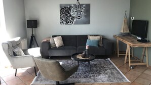 Ein modernes Wohnzimmer mit einem grauen Sofa, einem schwarzen Couchtisch und einem grauen Sessel. Ein großes Kunstwerk mit Leopardenmuster hängt an der Wand, und eine kleine Tischlampe steht auf dem Couchtisch.