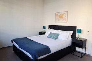 A neatly made bed with a blue blanket, two bedside tables with lamps, a framed picture on the wall, and a plain white wall. - Close to the Heart of Lugano (Mola Glicine) (Lugano)