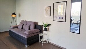 Un salon moderne avec un canapé, une lampe sur pied, une petite table sur laquelle est posée une plante, des œuvres d’art encadrées et un grand miroir.