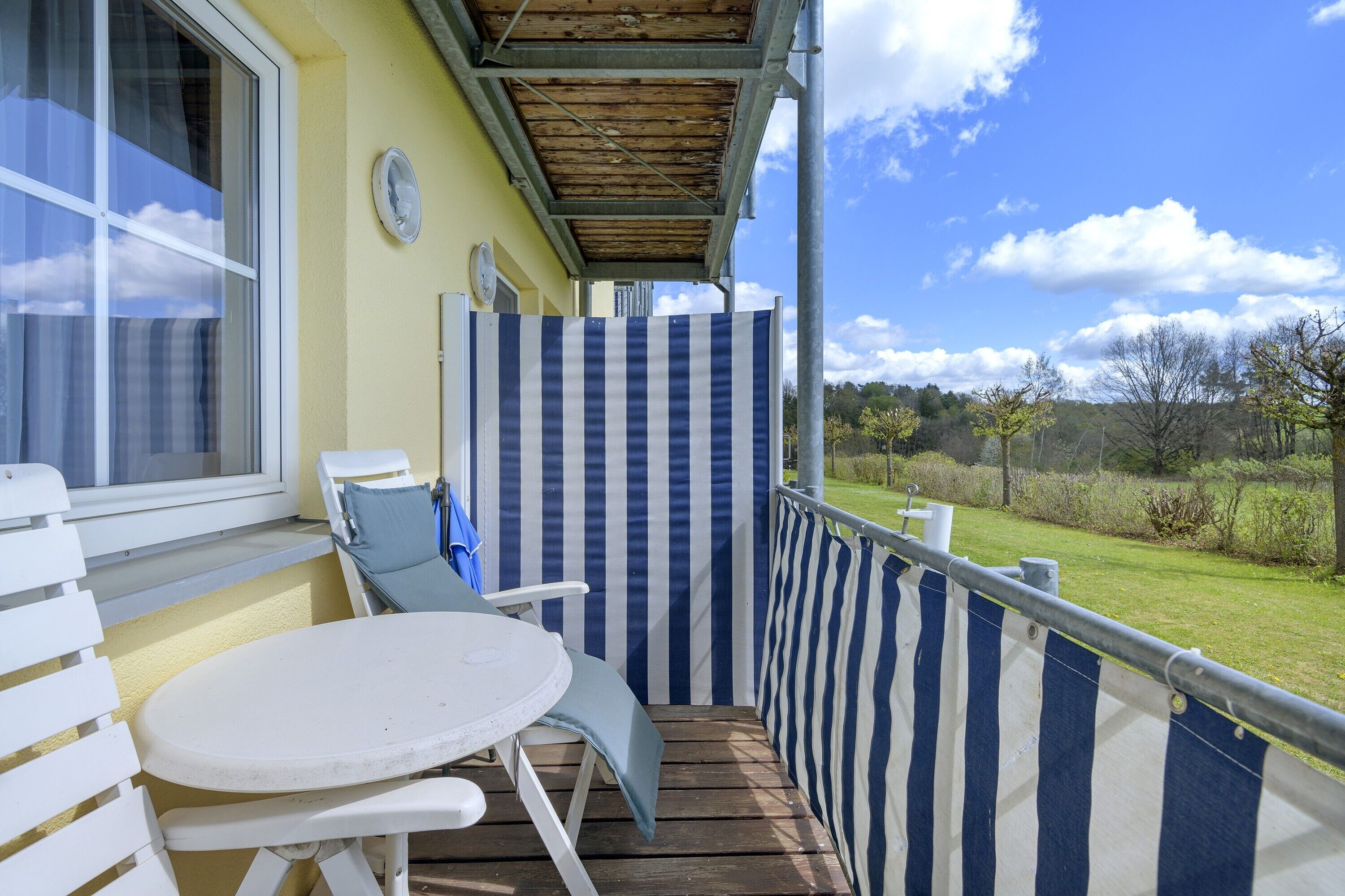 Ein Balkon mit Tisch und Stühlen, einem gestreiften Sichtschutz und Blick auf die Landschaft.