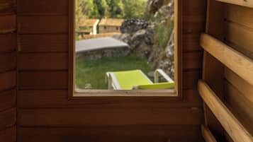 Una cabaña de madera con una ventana que da a un paisaje verde y un edificio.