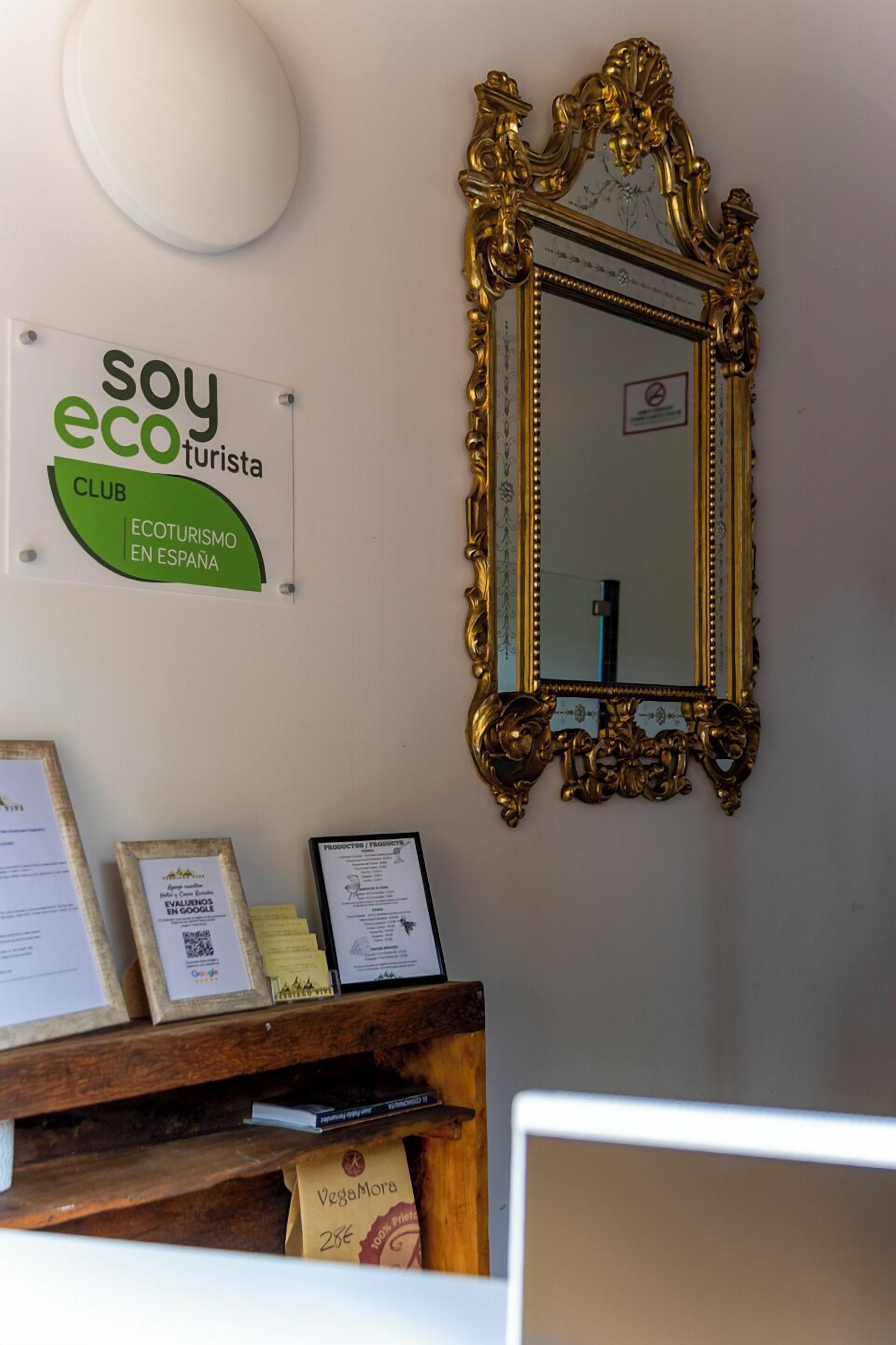 Una pared con un espejo enmarcado, un letrero que dice 'soy eco turista CLUB ECOTURISMO EN ESPAÑA', y documentos enmarcados en una estantería.