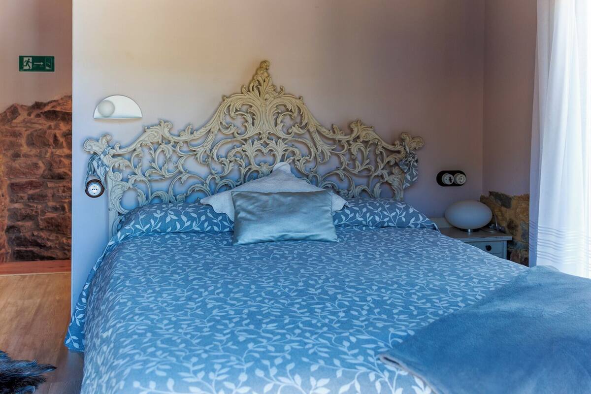 Une chambre à coucher avec un lit, une table de chevet, une lampe fixée au mur et un mur en pierre.