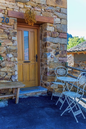 Un edificio de piedra con puerta de madera, con el número 20, y un pequeño espacio al aire libre con sillas de metal.