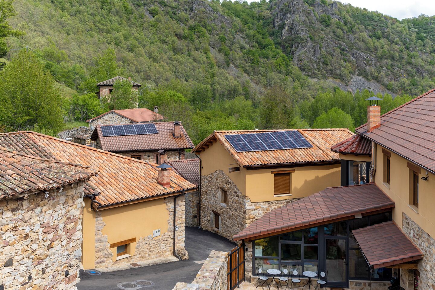 A hillside village with traditional stone and tiled buildings, some with solar panels.