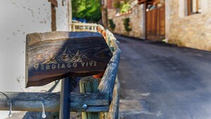 A wooden sign with the inscription "VERDIGO VIVE" and a mountain design, mounted on a post in a narrow street with stone buildings.