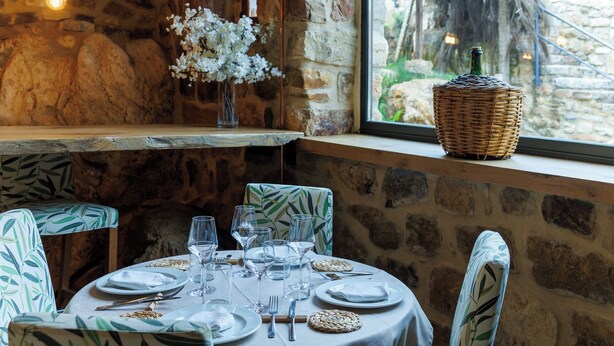 A dining area with a stone wall, a large window, and a table set for four with chairs.