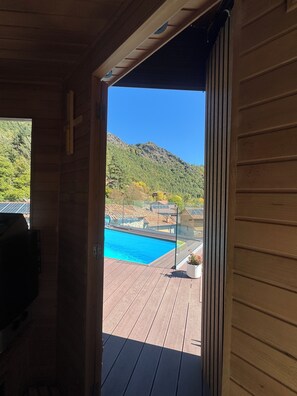 Una terraza de madera con piscina, vistas a la montaña y cielo despejado.