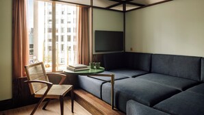 Un salon moderne avec un canapé, un fauteuil, une petite table sur laquelle sont posés des livres et des verres, et un téléviseur fixé au mur.