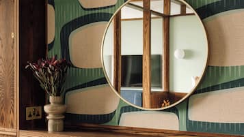 A wooden cabinet with a vase of flowers, a round mirror, and a patterned wall.