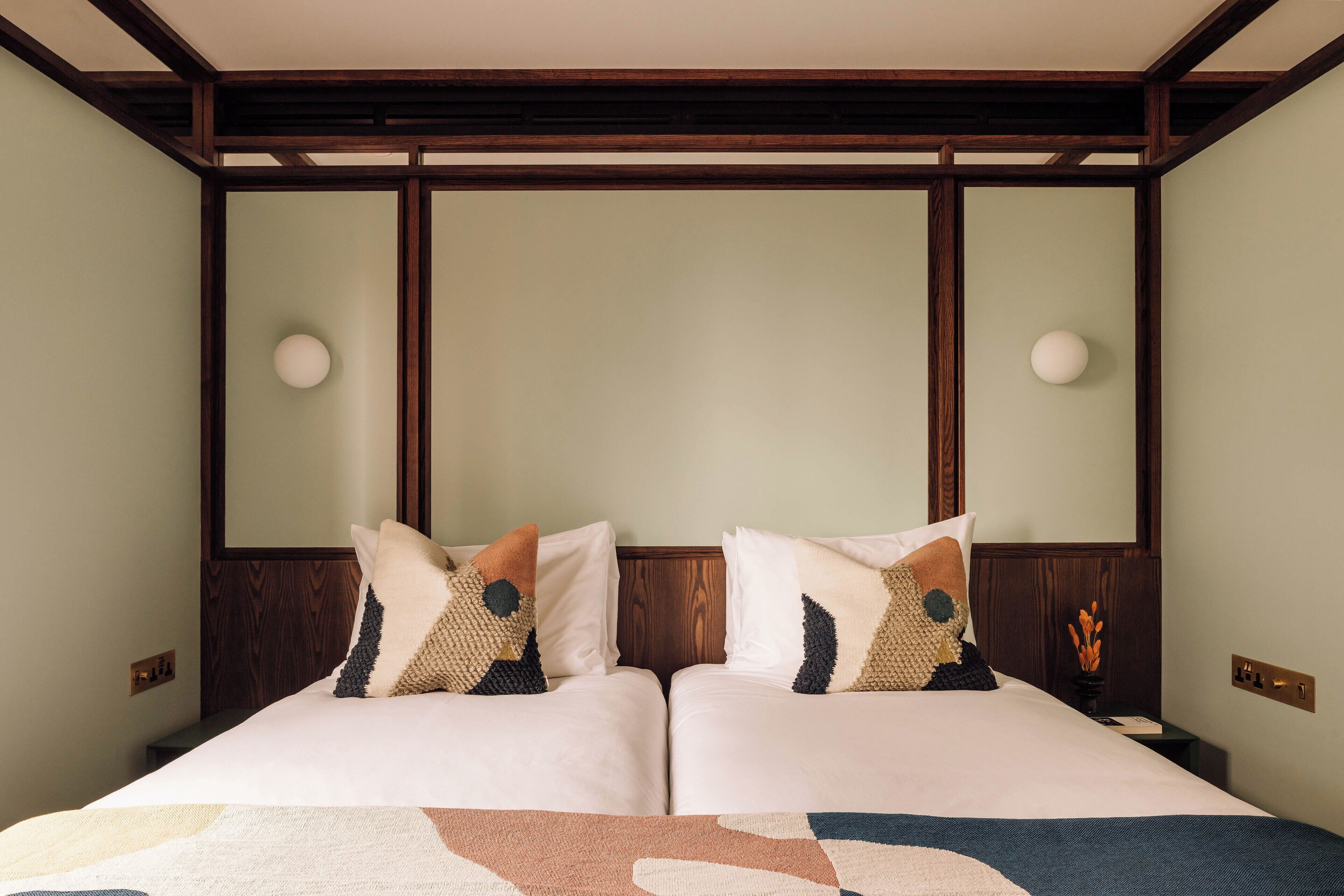 A double bed with a geometric-patterned bedspread, two pillows with a dog design, and a wooden headboard.