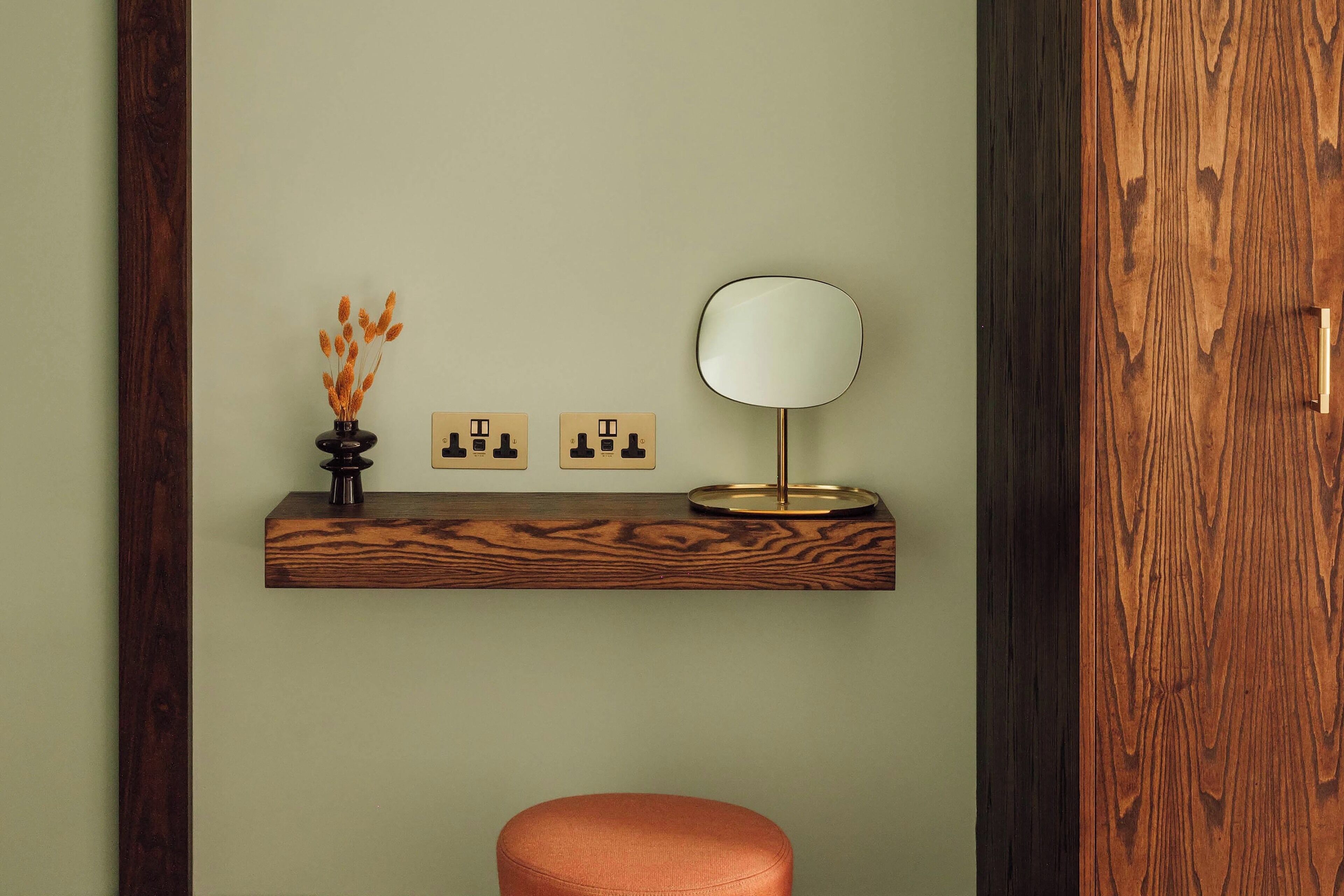 A bathroom with a wooden vanity, a round mirror, and a small vase with dried flowers.