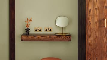 A bathroom with a wooden vanity, a round mirror, and a small vase with dried flowers.