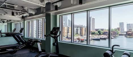 Une salle de sport équipée de matériel d’exercice et dotée de grandes fenêtres donnant sur un paysage urbain.