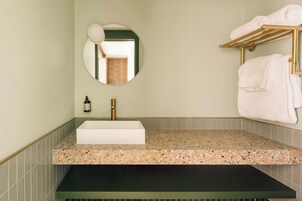 Un baño con un lavamanos rectangular, un espejo redondo y un toallero.