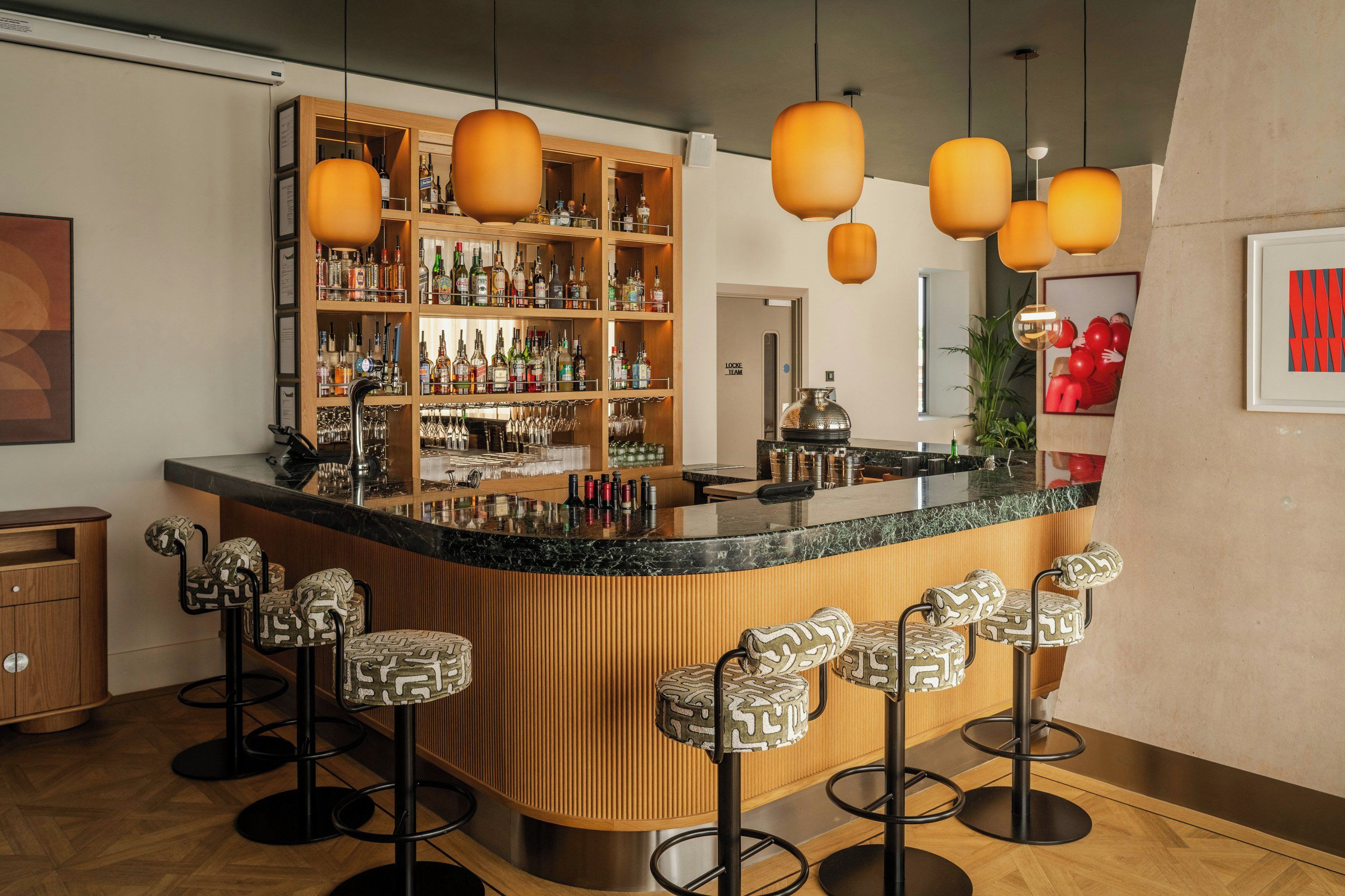 A bar area with a curved counter, multiple stools, and a shelving unit with bottles.
