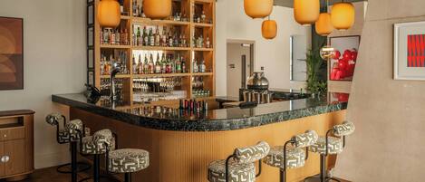 Una zona de bar con una barra curva, varios taburetes y una estantería con botellas.