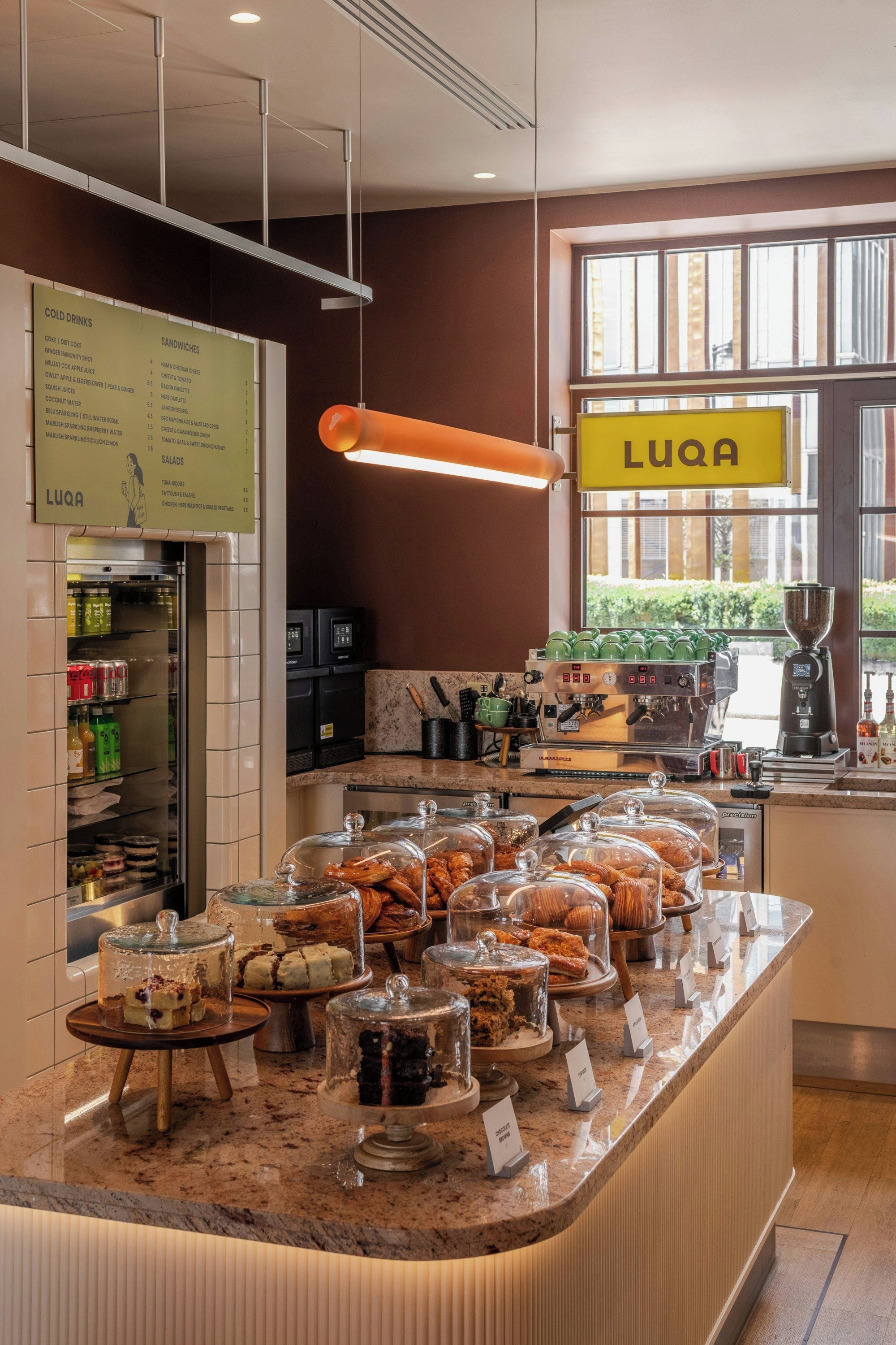 Un área de buffet con diversas opciones de comida, una máquina de café y un letrero que indica el nombre LUQA.