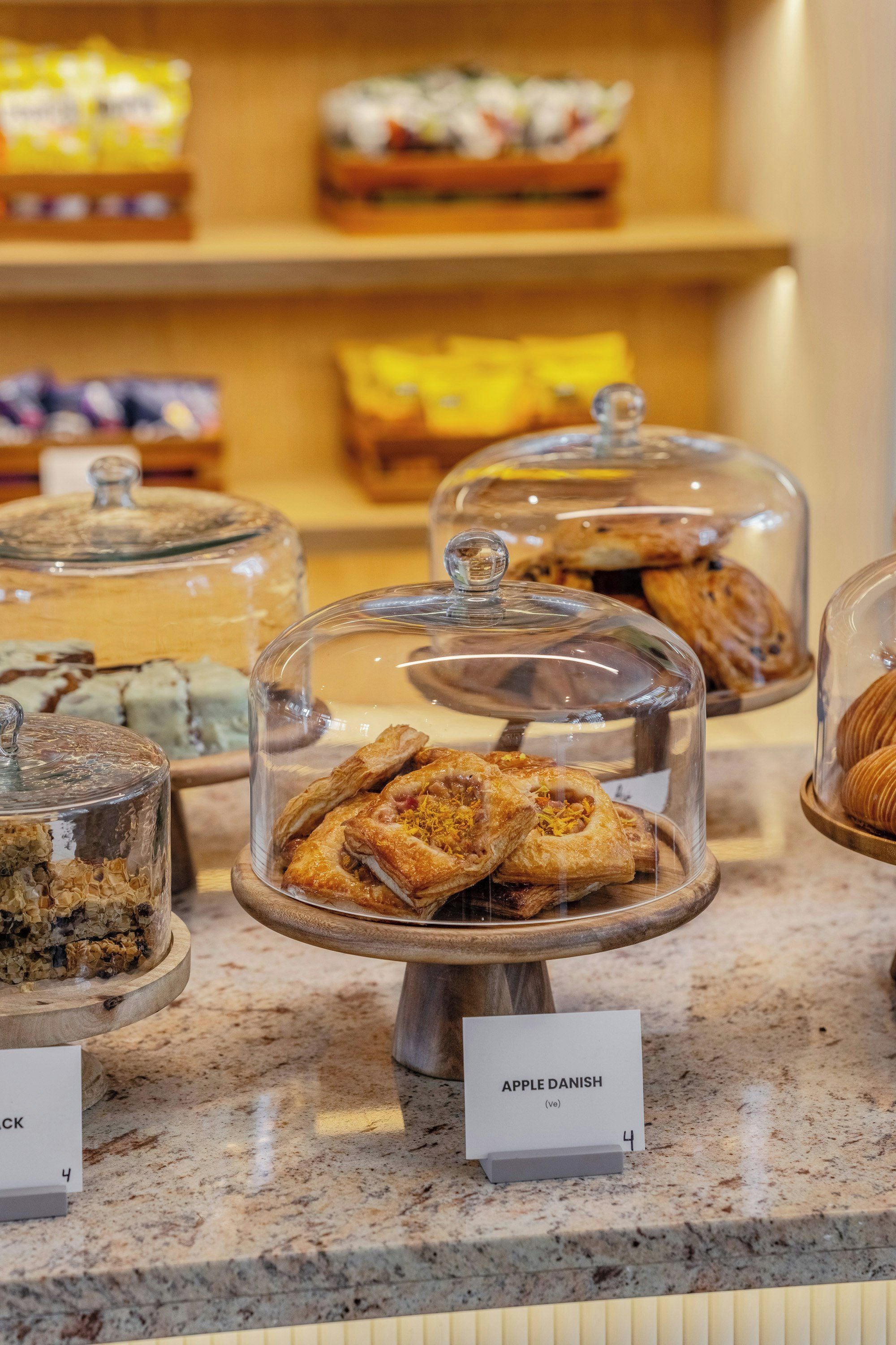 A bakery display with various pastries under glass domes, including a sign for 'Apple Danish.'