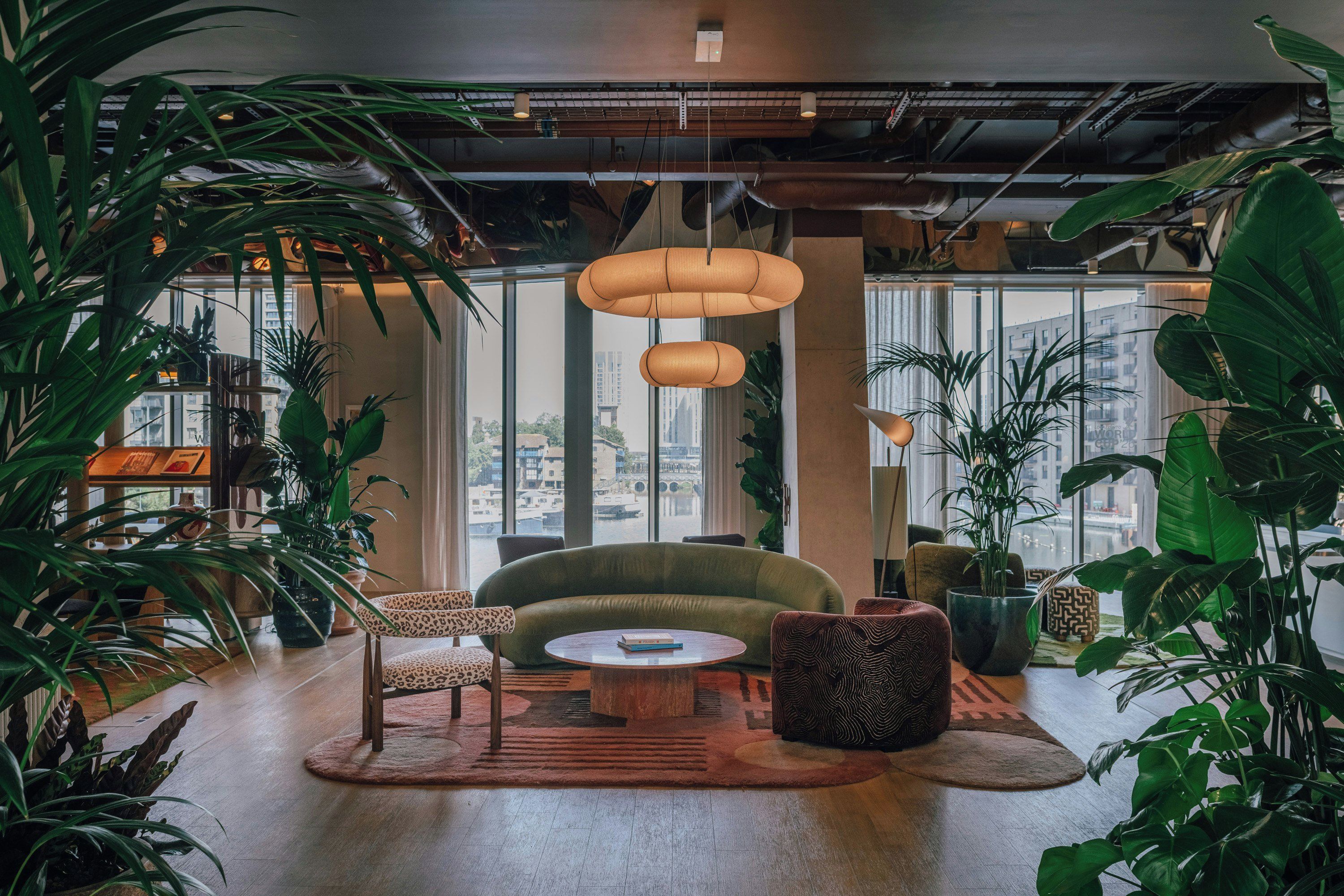 A modern interior with a green sofa, round wooden table, and various plants.