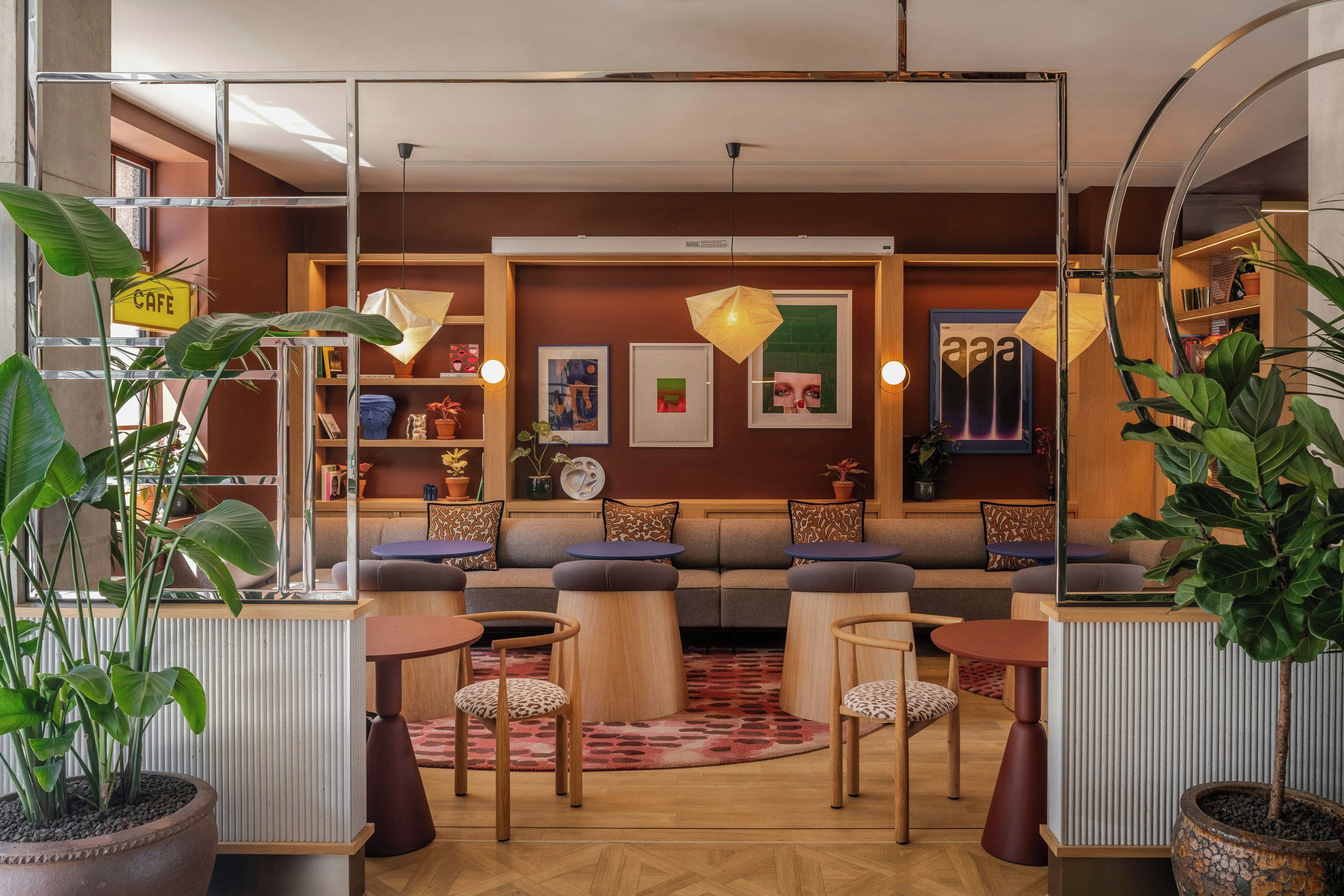 A modern lounge area with a sofa, chairs, and tables, featuring artwork and plants.