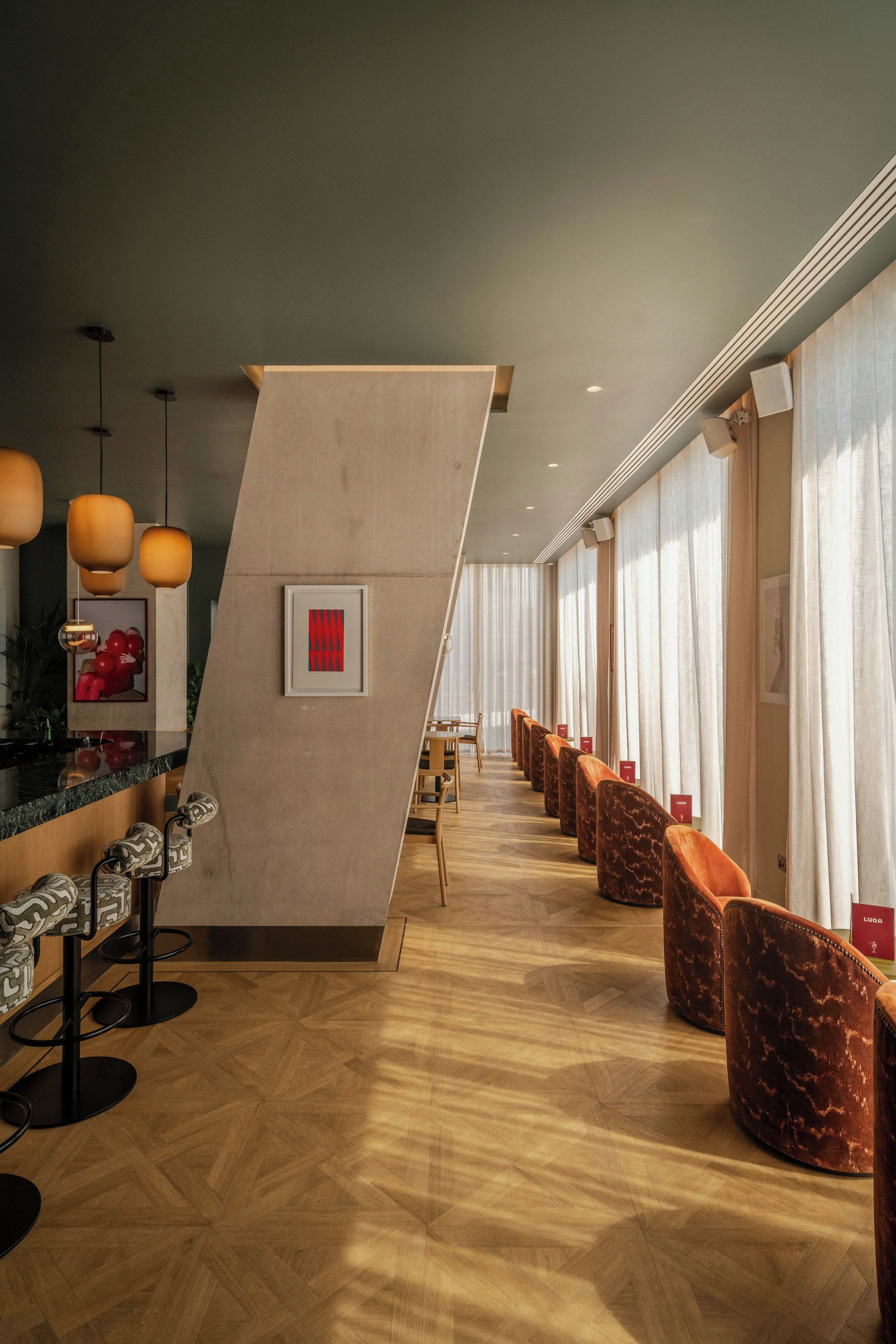 A modern hotel lobby with a wooden floor, a reception desk, and a seating area with cushioned chairs.