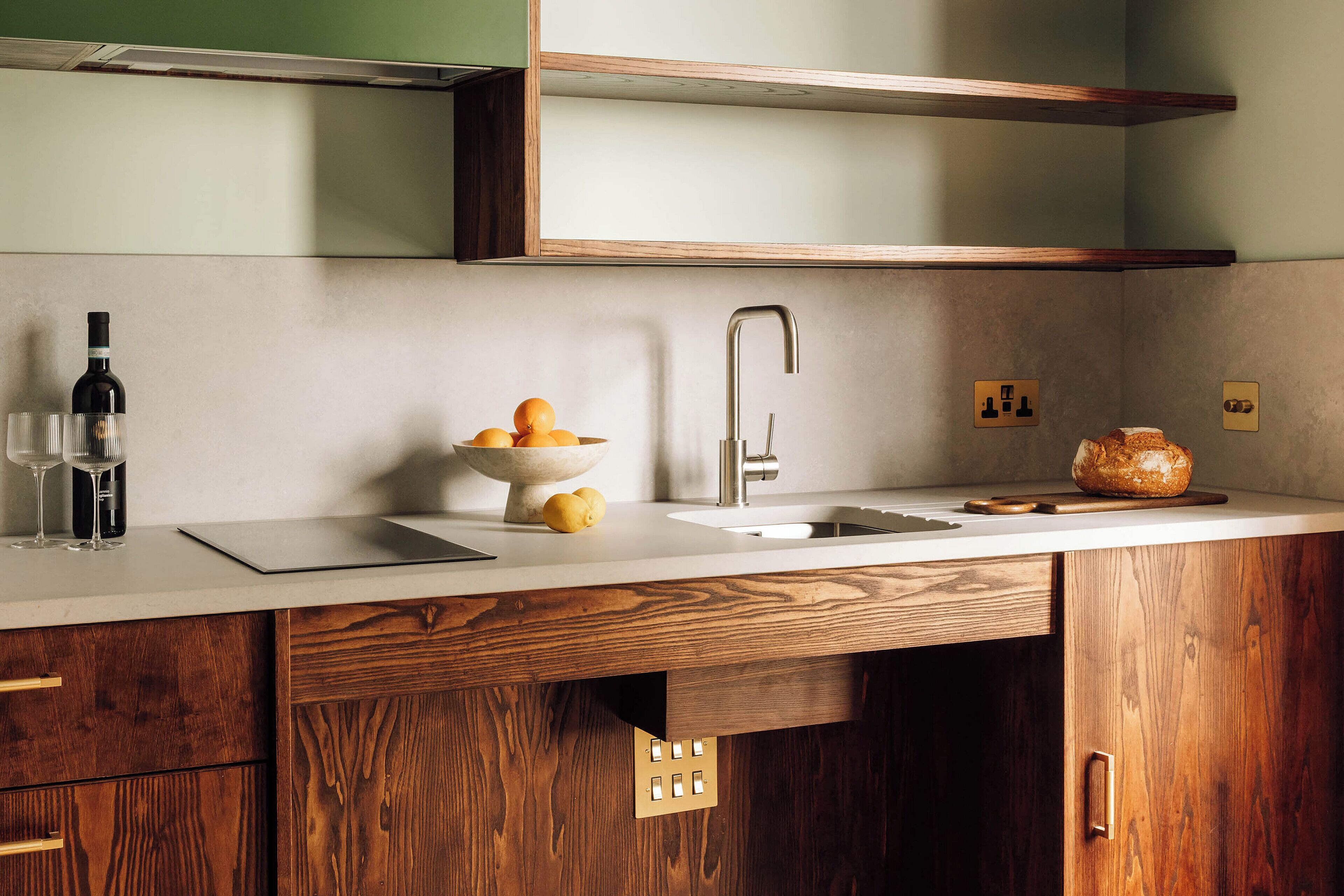 A modern kitchen with wooden cabinets, a white countertop, a stainless steel sink, and a bowl of oranges.