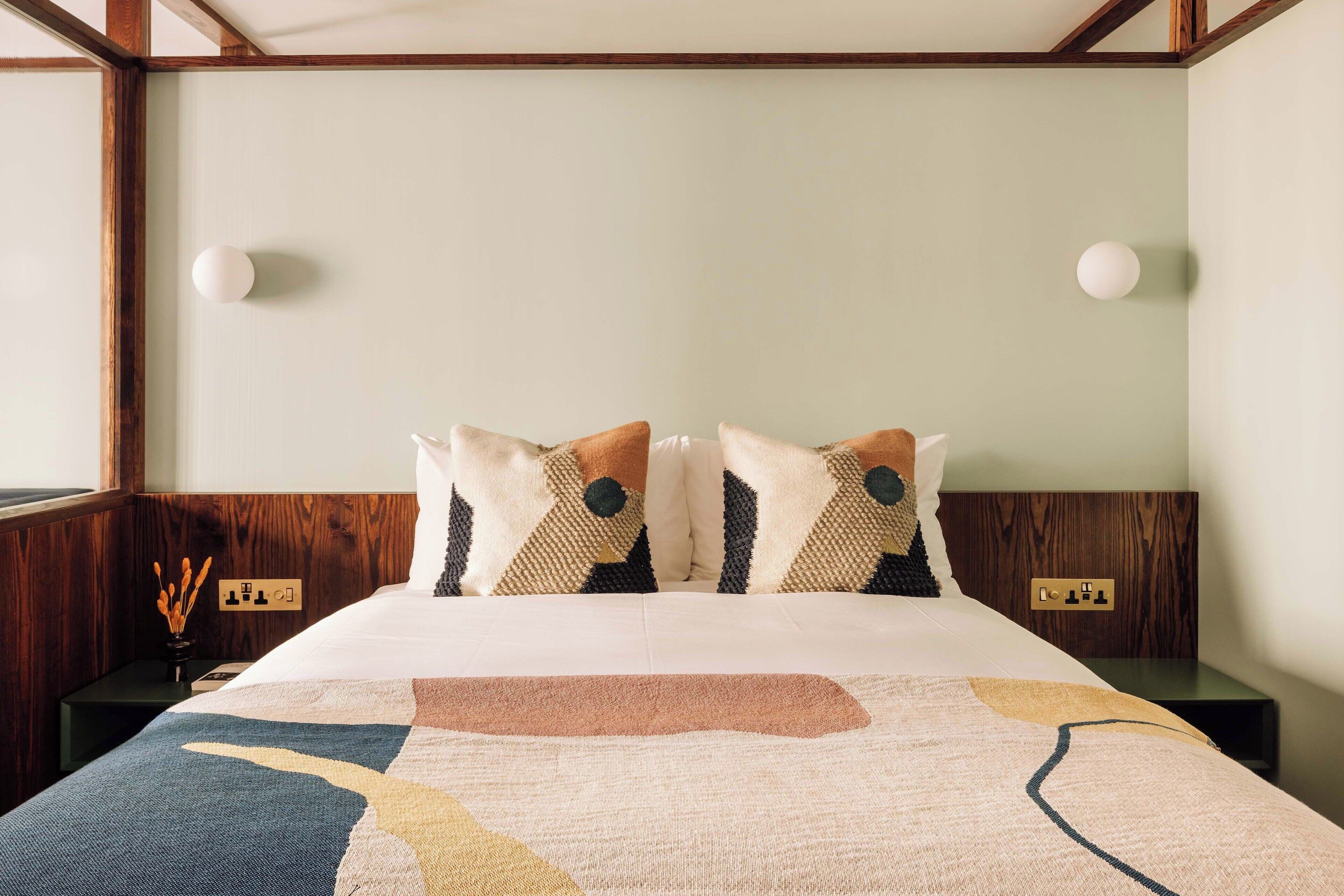 Un lit bien fait, avec une couverture à motifs géométriques, une tête de lit en bois et des lampes de chevet.