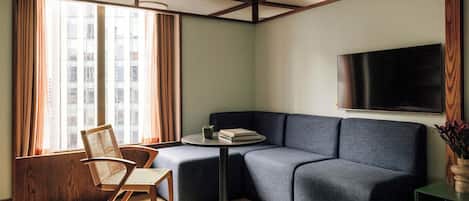 A modern living room with a sectional sofa, a round coffee table, and a flat-screen TV mounted on the wall.