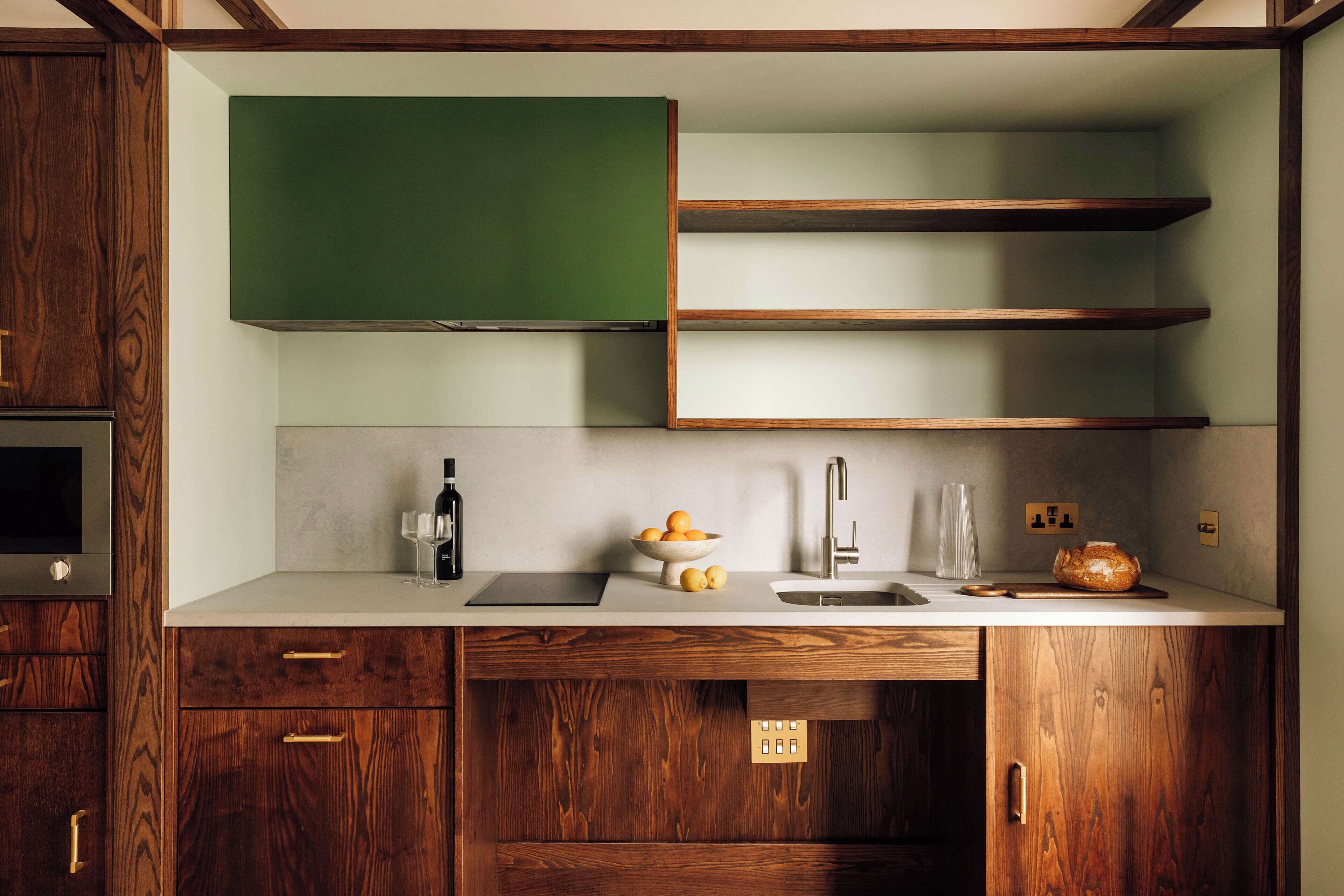 A modern kitchen with wooden cabinets, a green chalkboard, and a countertop with a sink, wine glass, and a bowl of fruit.