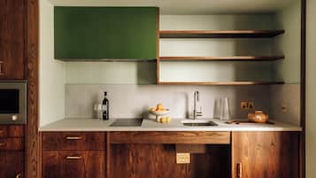 A modern kitchen with wooden cabinets, a green chalkboard, and a countertop with a sink, wine glass, and a bowl of fruit.