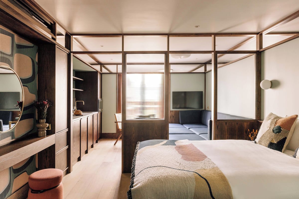 Ein modernes Hotelzimmer mit einem großen Bett, einem Schreibtisch mit Spiegel und einer Sitzecke mit Blick auf die Stadt.