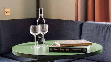 Une table ronde verte, sur laquelle sont posés deux verres à vin et une bouteille, est placée sur un canapé bleu foncé.