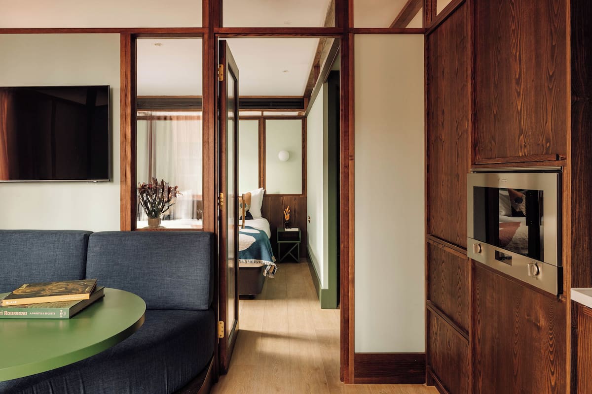 Ein modernes Hotelzimmer mit einer Couch, einem grünen Tisch, einem Bett und einem Holzschrank.